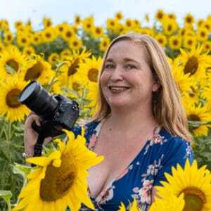 Portrait of a woman holding a camera in a field of sunflowers.