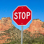 A red stop sign against a blue sky, with a red rocks on either side