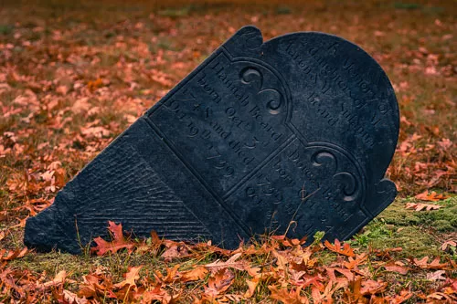 18th century grave stone, crooked, sunken into ground, surrounded by fall leave