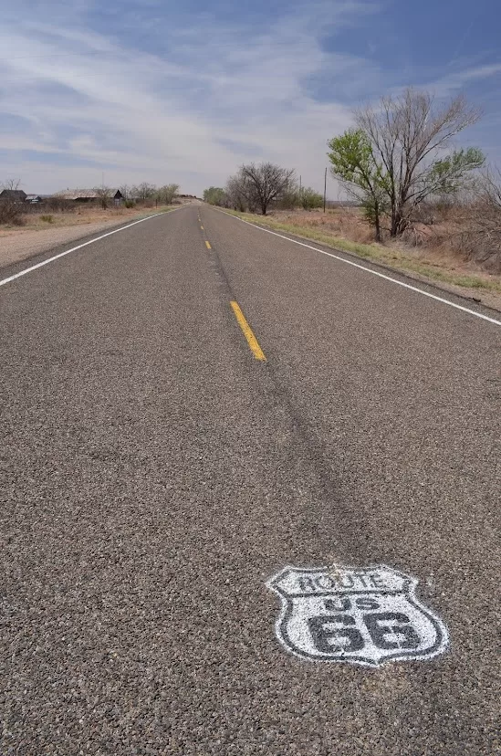 an empty road through the desert, the route 66 logo is painted on the pavement in the foreground