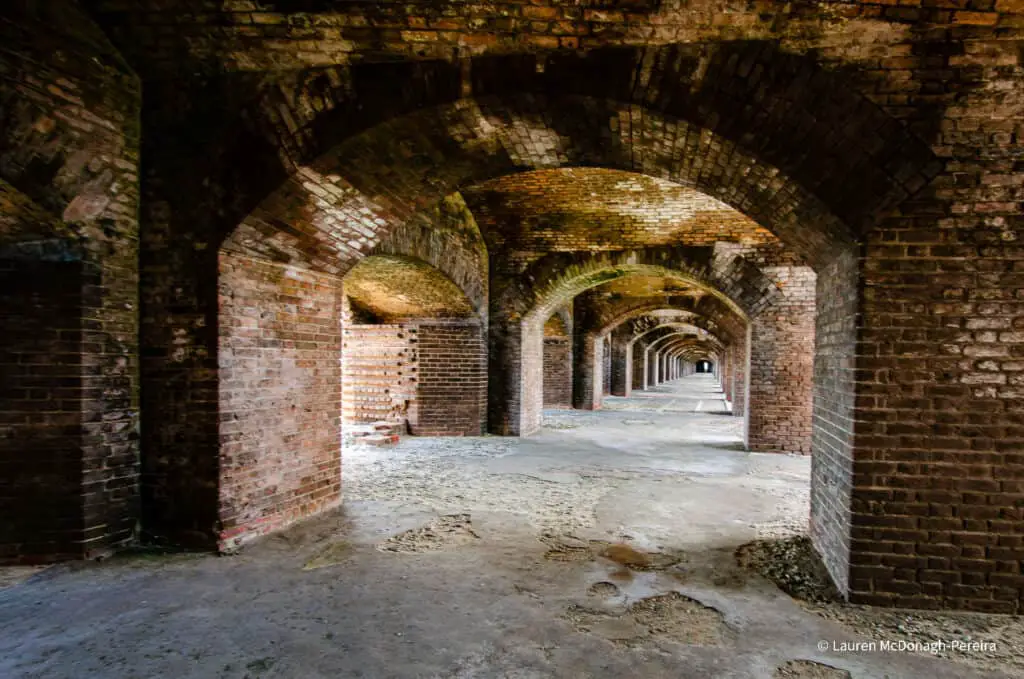 A path stretches through a 19-th century brick fort. The hallway is empty. A seemingly endless row of brick archways stretch to an infinity point.