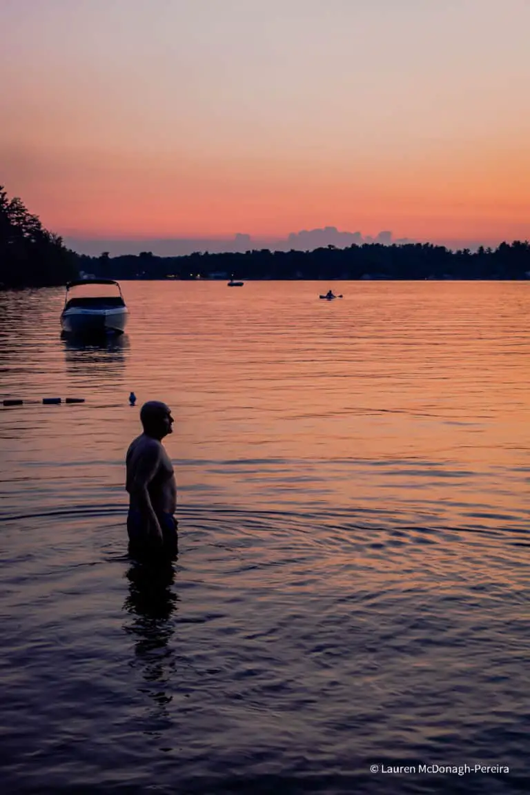 A man goes for a swim in a lake as the sunsets. He is cast in silhouette.